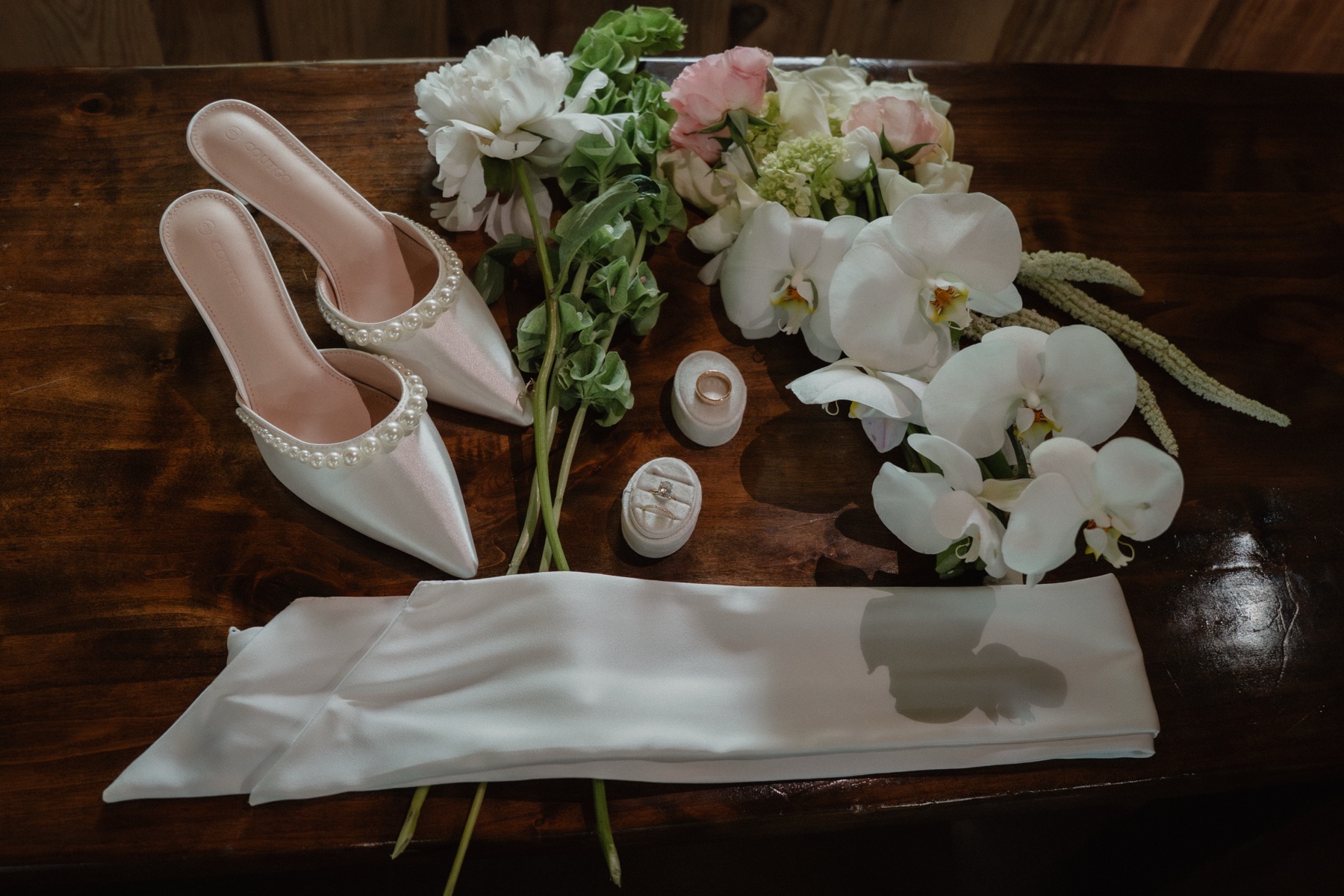Wedding shoes, florals, rings and silk ribbon flat-lay on a wood table