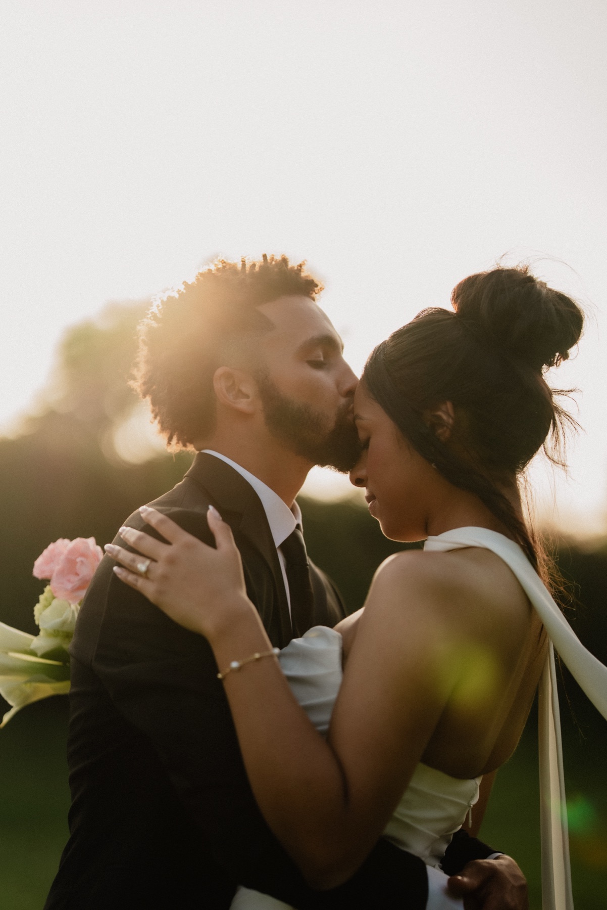 Couple shares a forehead kiss in soft golden hour light