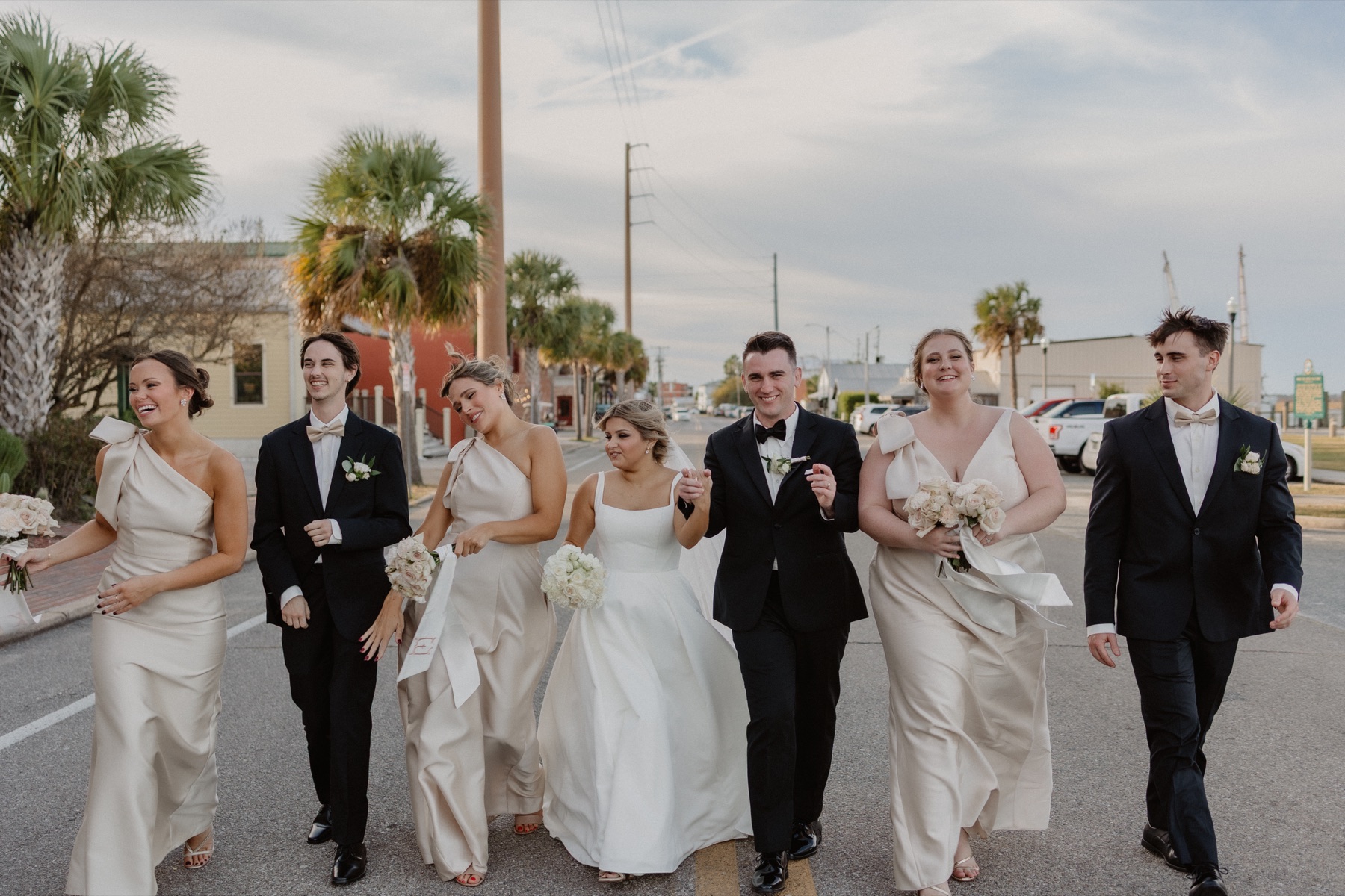 Wedding party walking together down a sunny coastal street in their formal attire